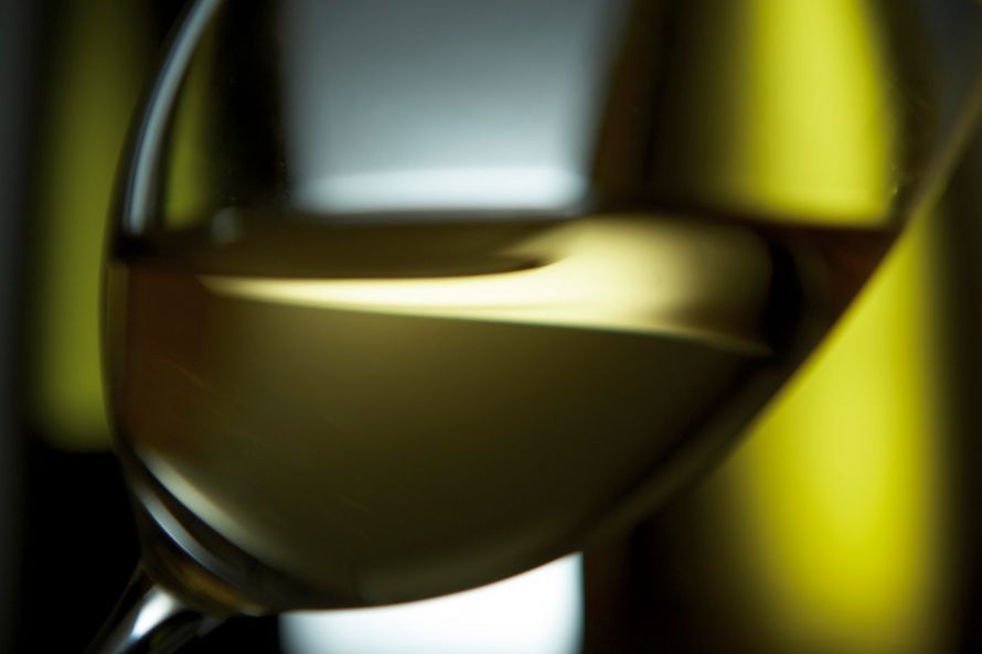 detail of glass of white wine with green bottles in background